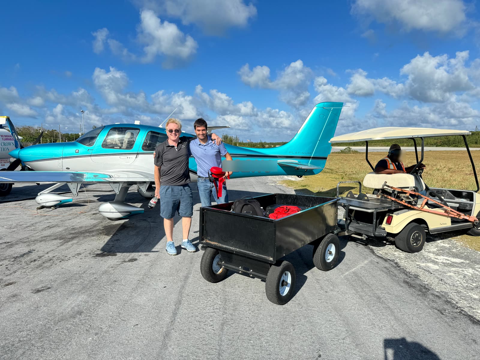 Instructor and owner beside a teal Cirrus SR22 at a Bahamas island airstrip with a loaded luggage cart