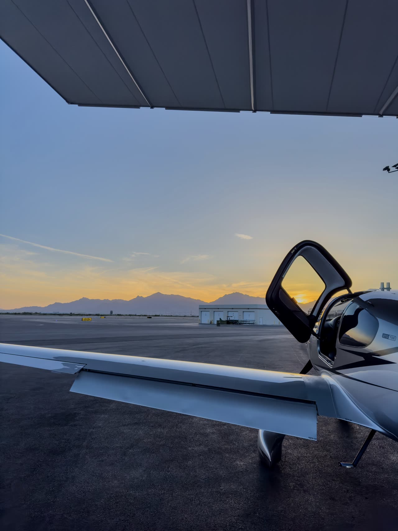Cirrus wing and open door at sunset on a desert ramp with mountains beyond